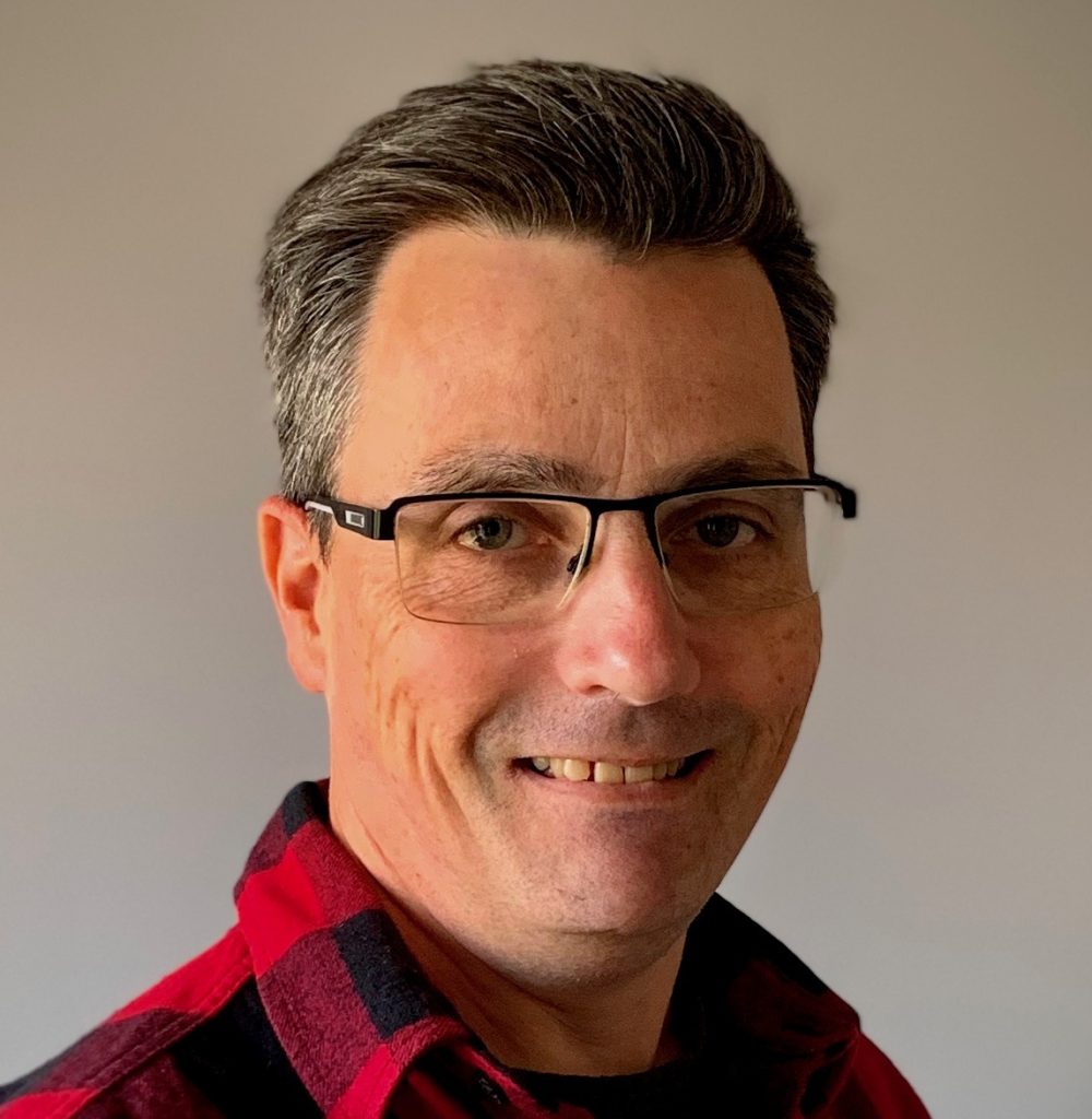 Middle aged man with dark and greying hair, smiling